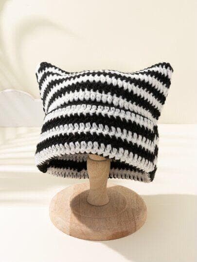 Bonnet crocheté à oreilles de chat, rayé noir et blanc, posé sur un support en bois.