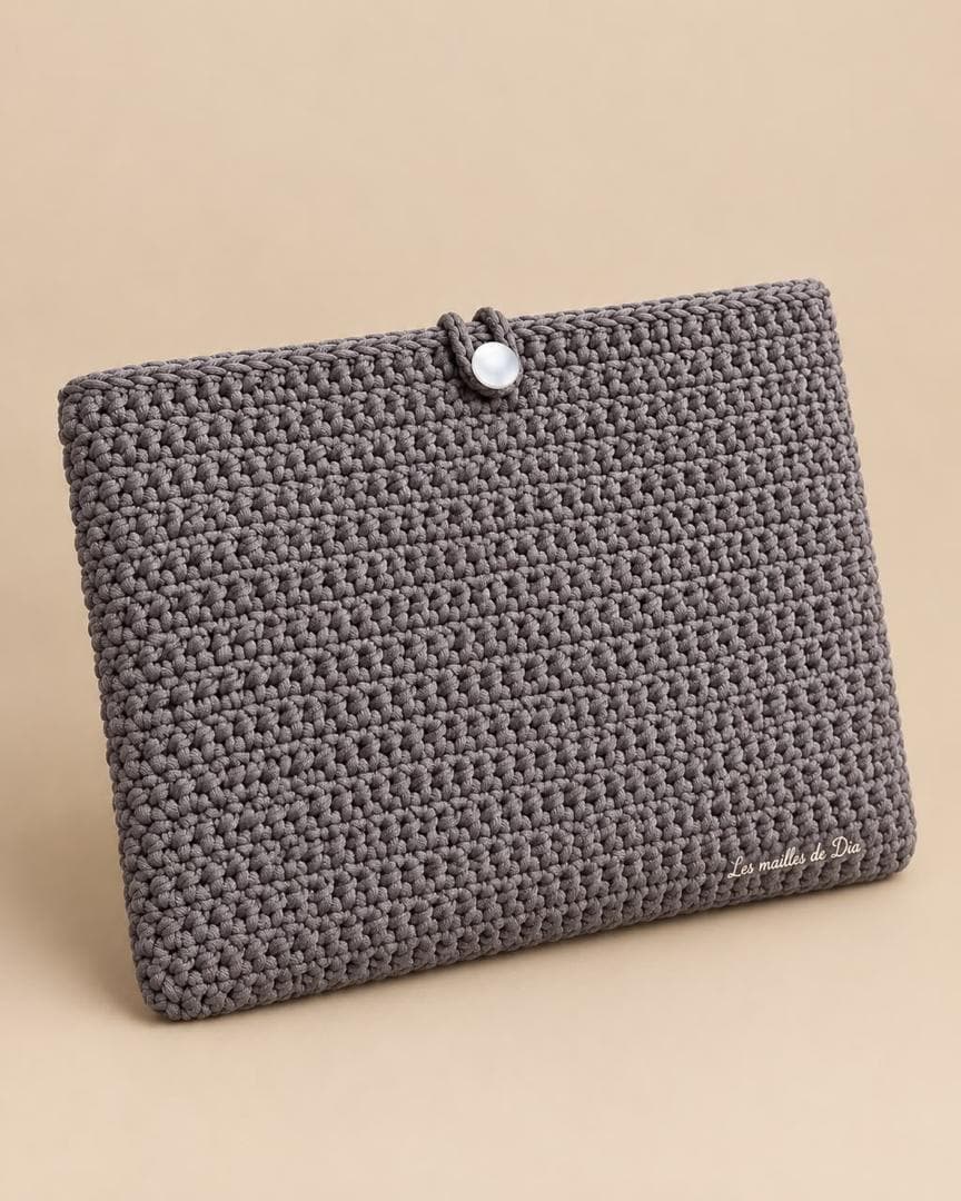 Housse d’ordinateur crochetée gris taupe, fermée par un bouton nacré.