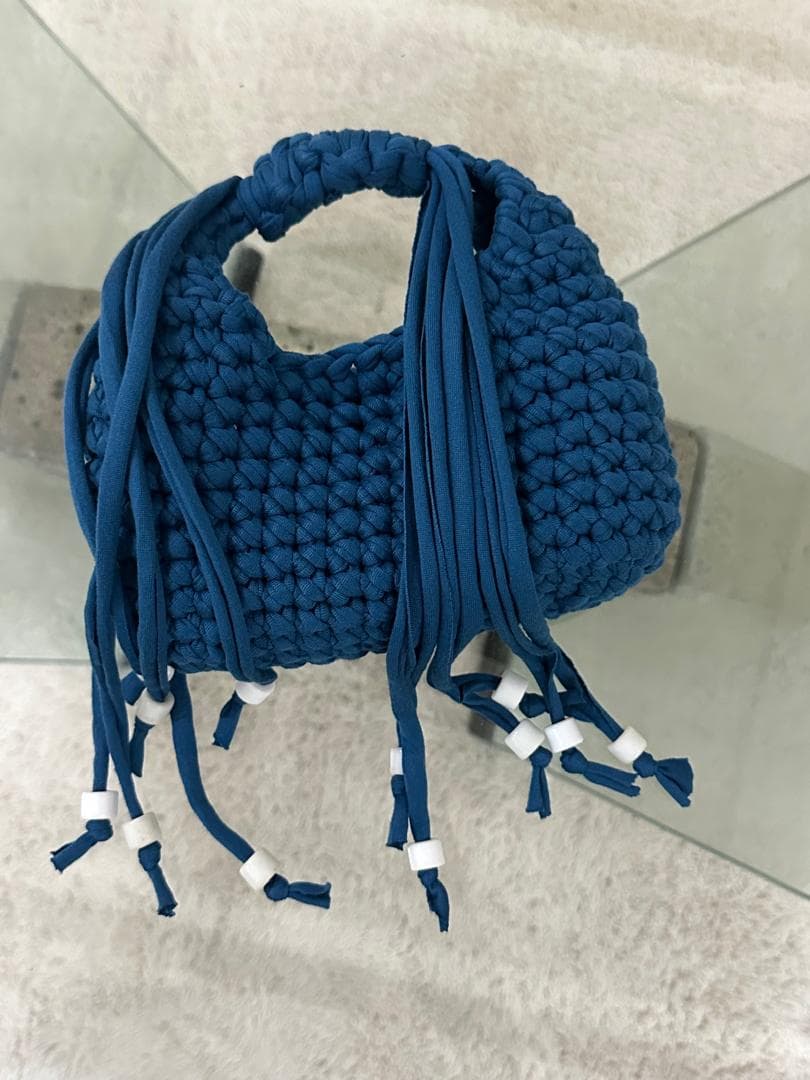 Sac crocheté bleu orné de franges terminées par des perles blanches.